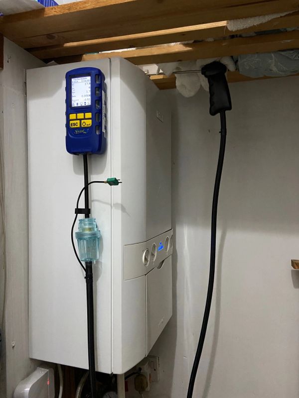 A white boiler with a blue digital device attached on top, mounted in a utility room.