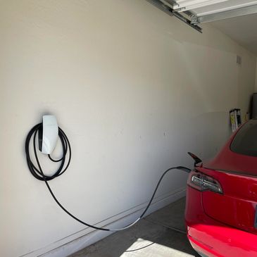 A red Tesla car charging in a garage with a Tesla wall charger.