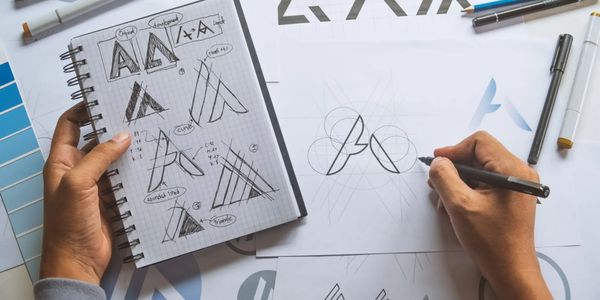 Person designing and sketching logo concepts with tools and markers.