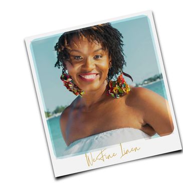 Smiling woman with colorful earrings by the water, wearing a white strapless top.