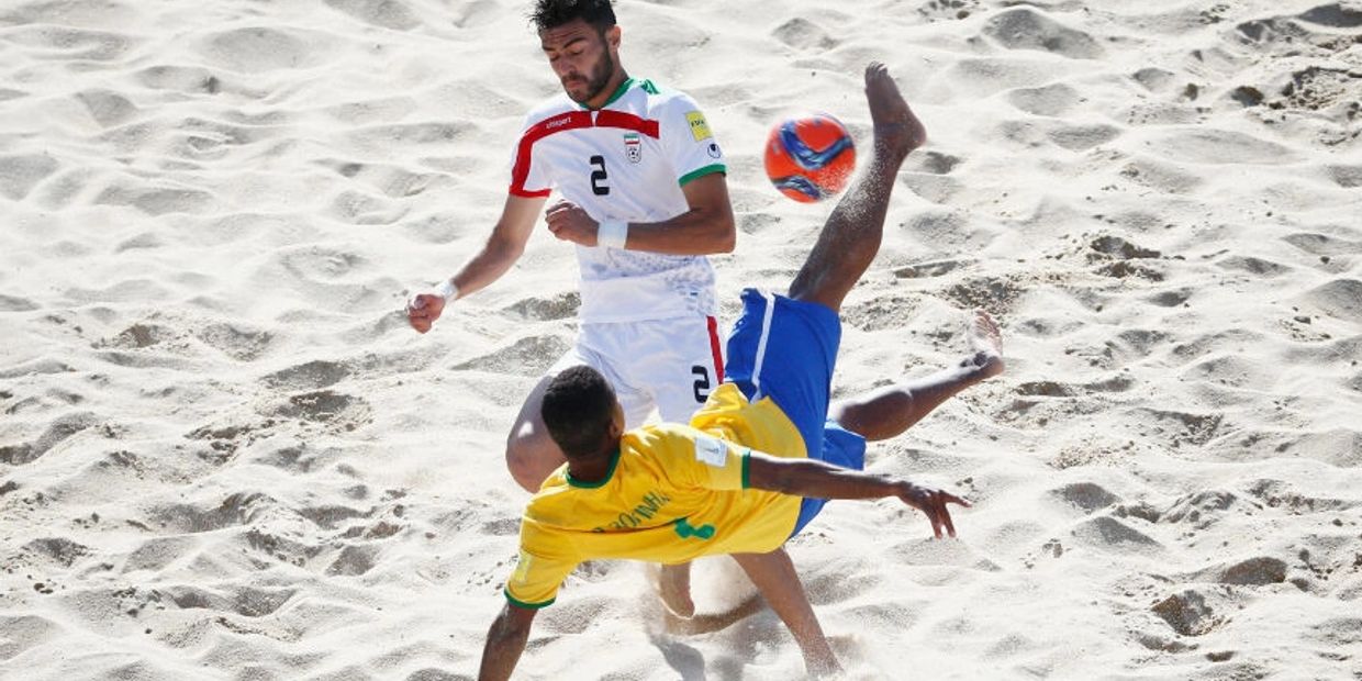 Two beach soccer players in action, one performing a bicycle kick.