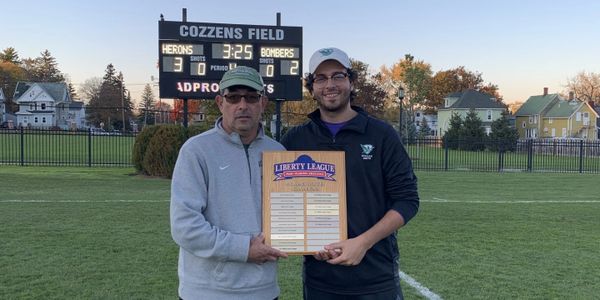 Two men holding a Liberty League championship plaque on a soccer field.