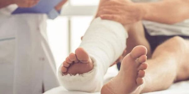 A patient with a wrapped right lower leg sits on a bed while a wound care provider stands bedside.