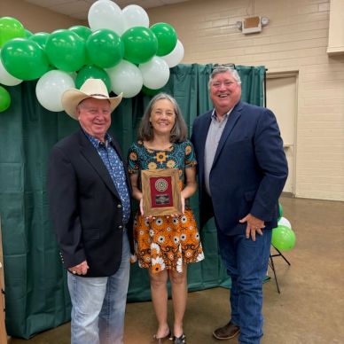 Three people posing with an award plaque in front of green and white balloons.