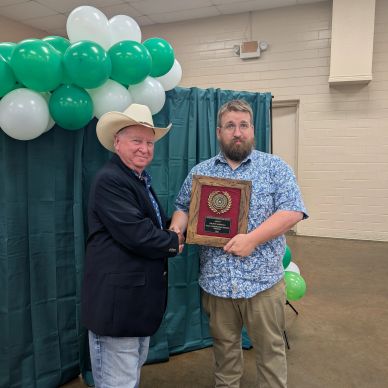 Man in cowboy hat shakes hands while another holds an award plaque.