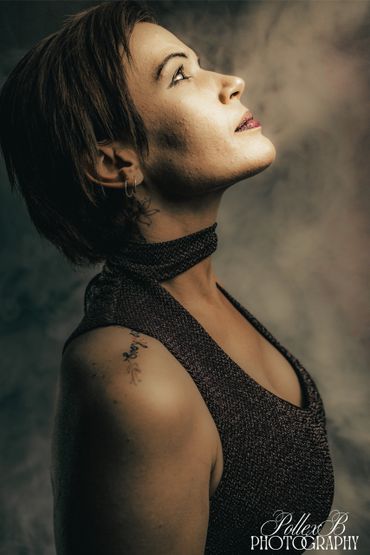 Profile of a woman with tattoos looking upward in a dark, textured outfit.