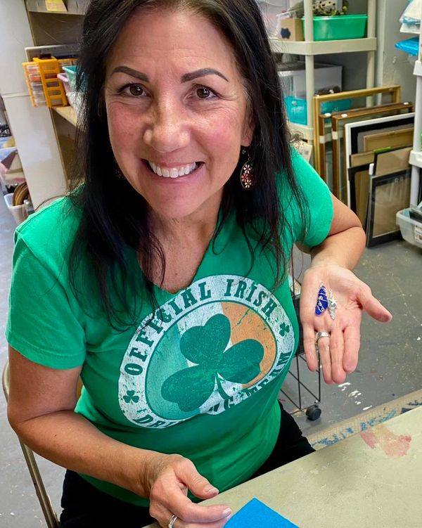 Smiling woman in a green 'Official Irish' shirt holding a small blue object in her hand.