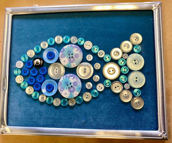 Fish shape made from various blue and white buttons framed on a teal background.