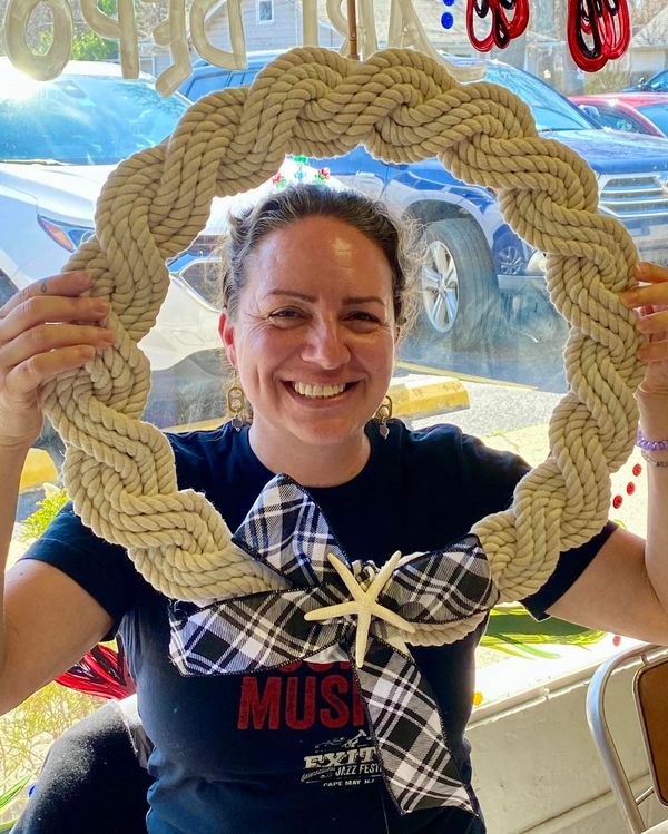 Smiling woman holding a decorative nautical rope wreath with a plaid bow and starfish.