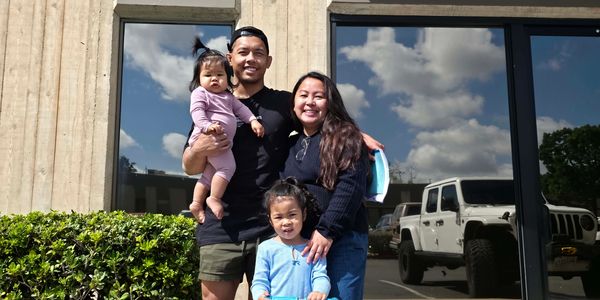 A happy family of four posing outdoors on a sunny day.