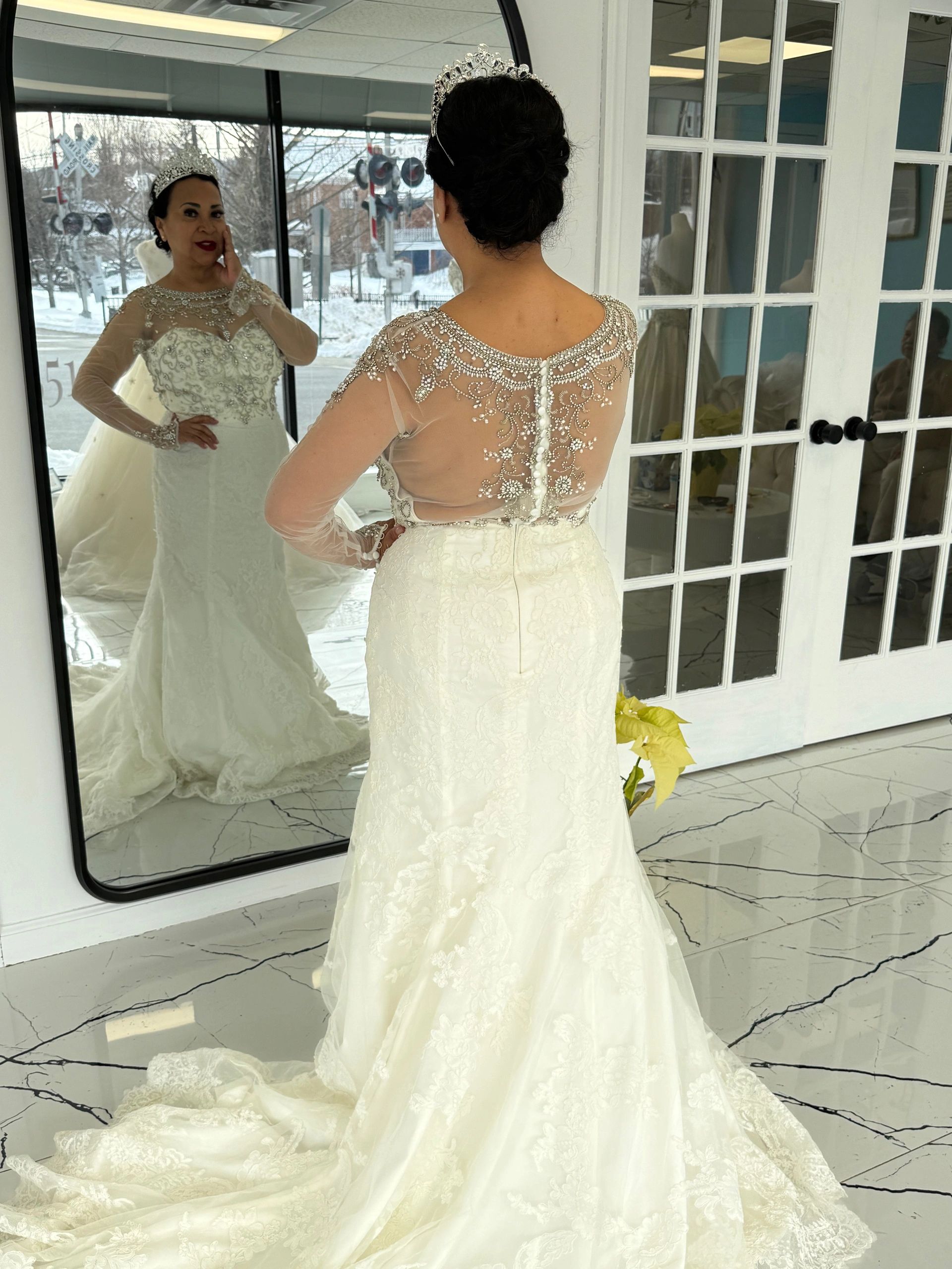 Woman in an elegant wedding dress admiring herself in a mirror indoors.