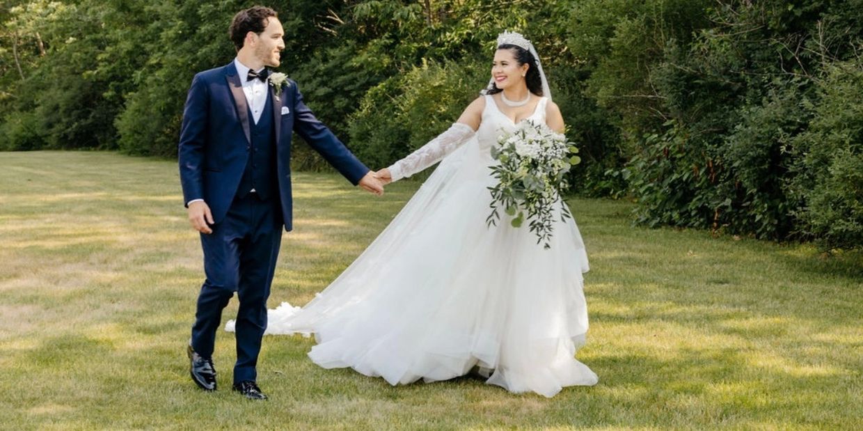 Bride and groom holding hands and smiling in a lush green outdoor setting.
