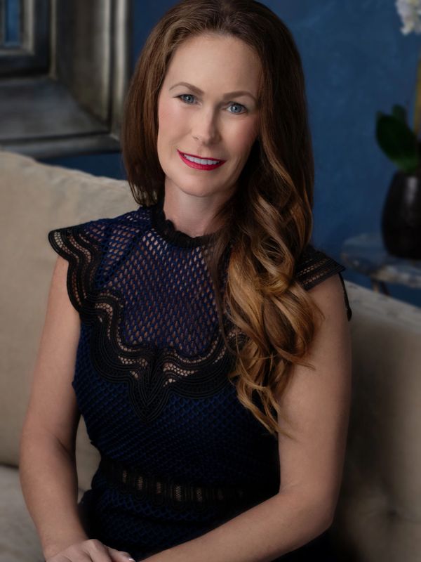 A woman with long wavy hair smiling, wearing a navy blue lace dress.