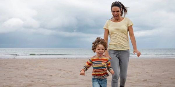 Mother and child joyfully running on a cloudy beach.