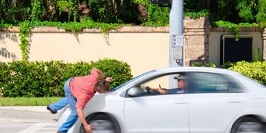 Person stumbling in front of a moving white car on a street.