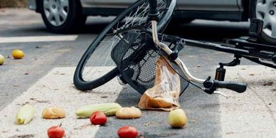 Bicycle overturned on street with scattered groceries nearby.