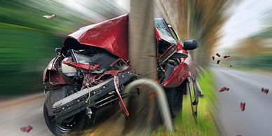 A red car crashed heavily into a tree, showing severe front-end damage.