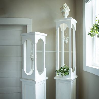 Two white decorative plant stands with intricate designs in a bright room.