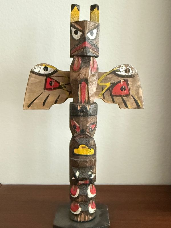 Wooden totem pole with painted animal faces and wings.