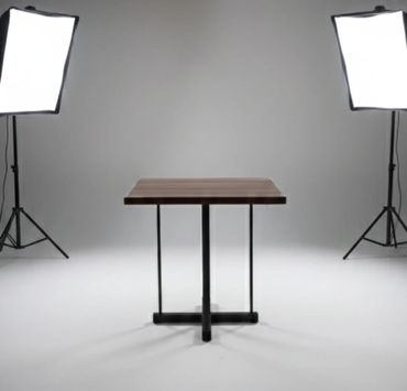 A wooden table centered between two studio lights in a white room.