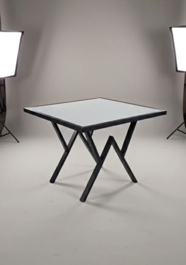 Modern square table with unique angular black legs and white top in a studio.