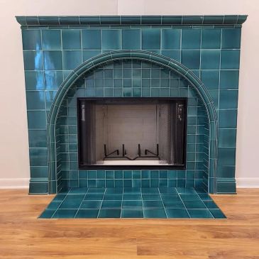 A stylish fireplace with teal tiles and wooden flooring.