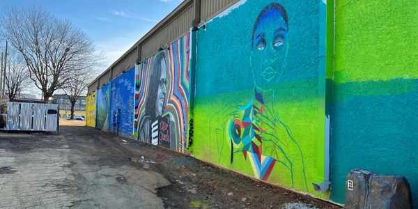Colorful mural of faces on an urban wall along a street.