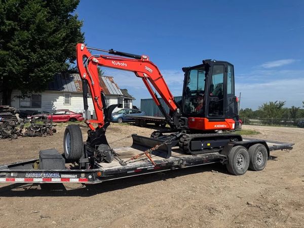 Orange Kubota KX40 Mini excavator loaded on a flatbed trailer outdoors.