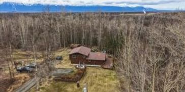 A cabin surrounded by bare trees with snowy mountains in the background.