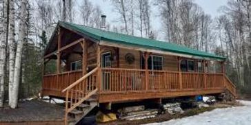 Cozy wooden cabin with green roof in a snowy forest setting.