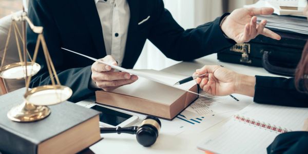 Two professionals discussing documents in a legal setting with scales and a gavel.
