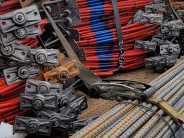 Stacked construction metal rods and clamps with red and blue cables.