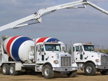 Two white cement mixer trucks with red and blue stripes are parked on a dirt surface.