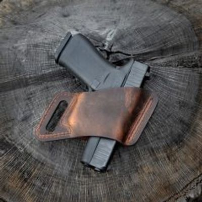 Black handgun partially covered by a brown leather holster on a tree stump.