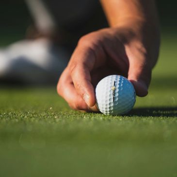 Hand placing a golf ball on the grass.