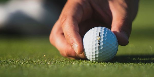 Hand placing a golf ball on the grass.