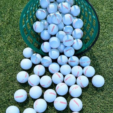 Golf balls spilling from a green basket onto grass.