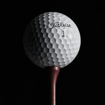 Close-up of a Titleist golf ball on a tee against a black background.