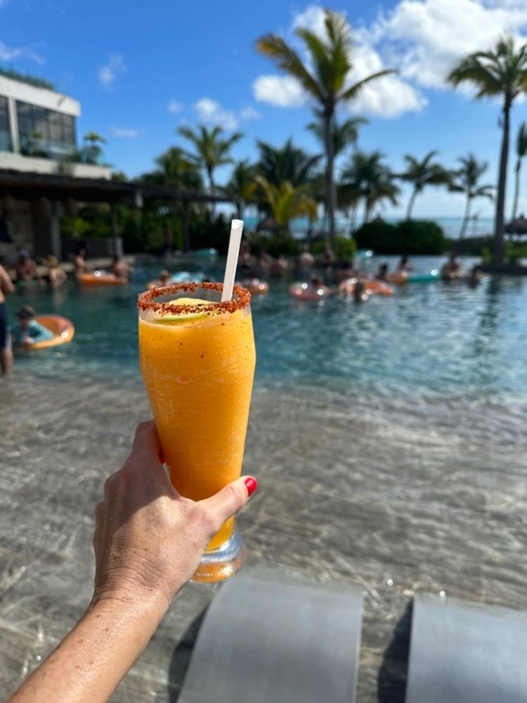Refreshing orange cocktail held by a pool with palm trees and blue skies.