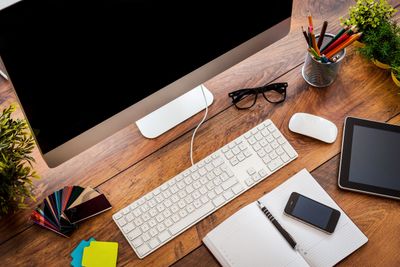 A tidy wooden desk with computer, keyboard, glasses, phone, and stationery.