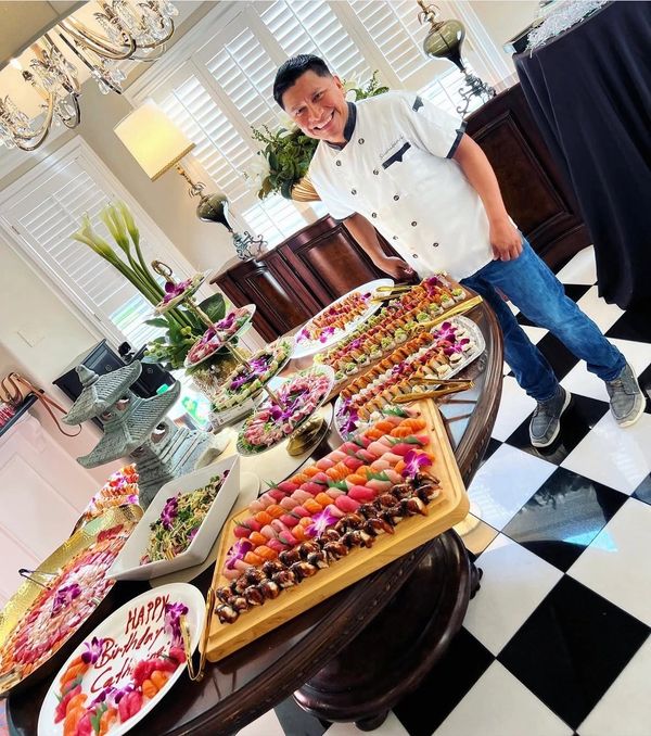 Chef proudly stands by an elaborate sushi and seafood spread for a birthday celebration.