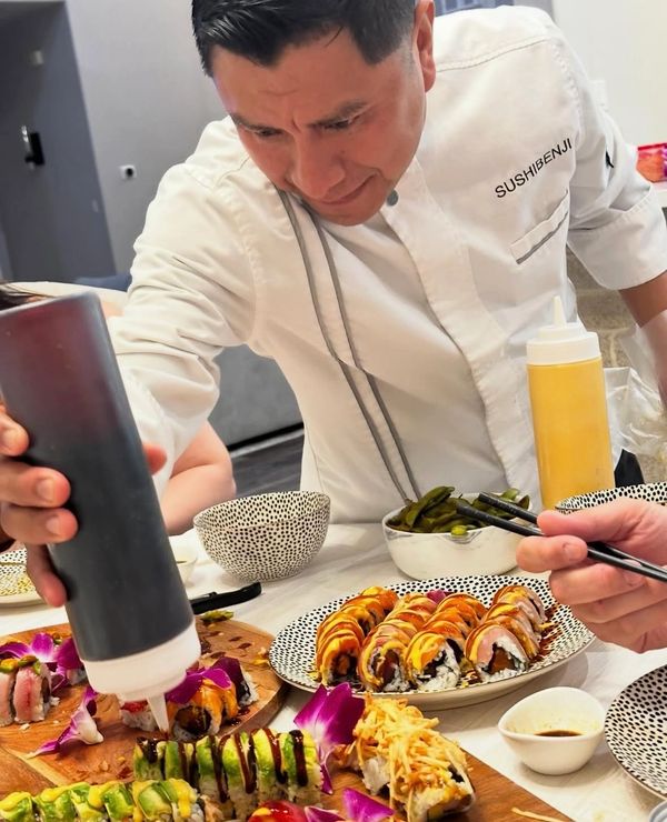 Chef drizzling sauce on sushi rolls at a vibrant sushi table.