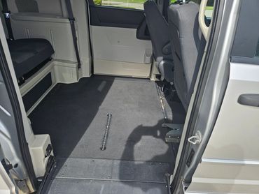 Empty wheelchair-accessible van interior with foldable seats and secure floor tracks.