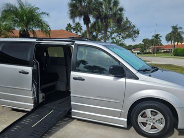 Silver wheelchair accessible van with ramp deployed on driveway.