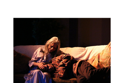 An elderly woman comforts a young man resting on her lap on a couch.