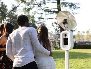 Three people using an outdoor photo booth on a sunny day.