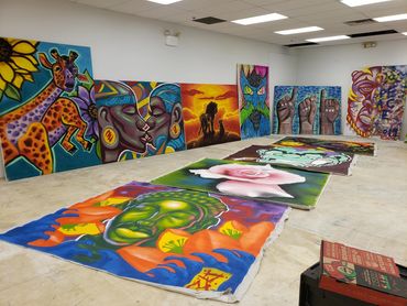 Colorful paintings laid out on the floor and against the wall in an art studio.