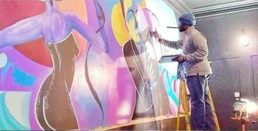 Artist painting a vibrant mural on a wall indoors.