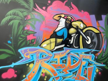 Colorful graffiti of a bearded man riding a yellow motorcycle with vibrant background and 'RIDE' text.