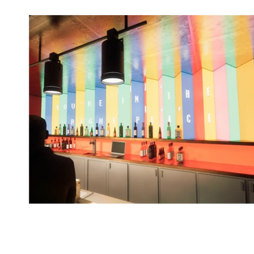 Colorful bar with bottles and neon sign reading 'You're in the right place'.